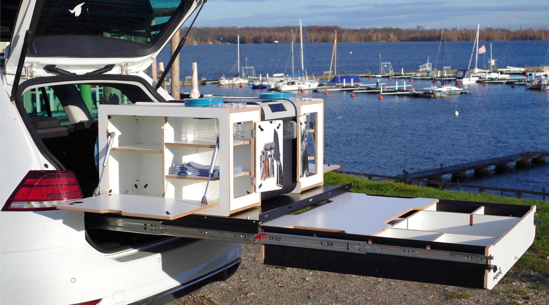 Ausgezogener Kofferraumauszug mit modularer Campingbox und integrierter Campingküche von SQUIQ – kompakte Outdoor-Küchenlösung im Auto am See