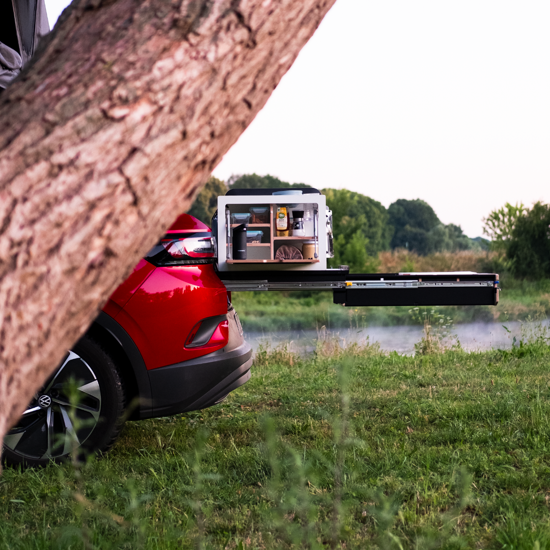 Uitschuifsysteem in een SUV met campingboxen in het groen voor een boom