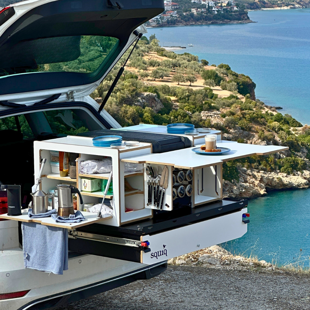 Campingbox in de kofferbak van een auto met camping-accessoires en uitzicht op de blauwe zee