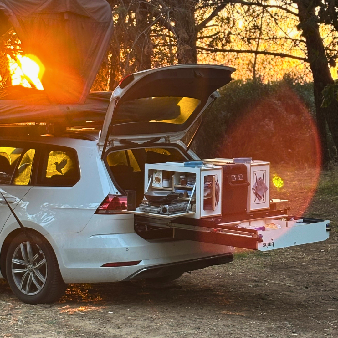 Campingbox im Kofferraum eines Autos mit Dachzelt bei Sonnenuntergang im Wald