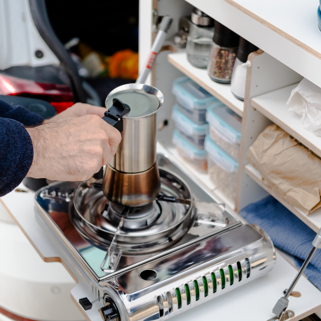 Campingbox in de kofferbak met inlegbodems, campingkooktoestel, kruiden en Tupperbakjes voor camperen met de auto