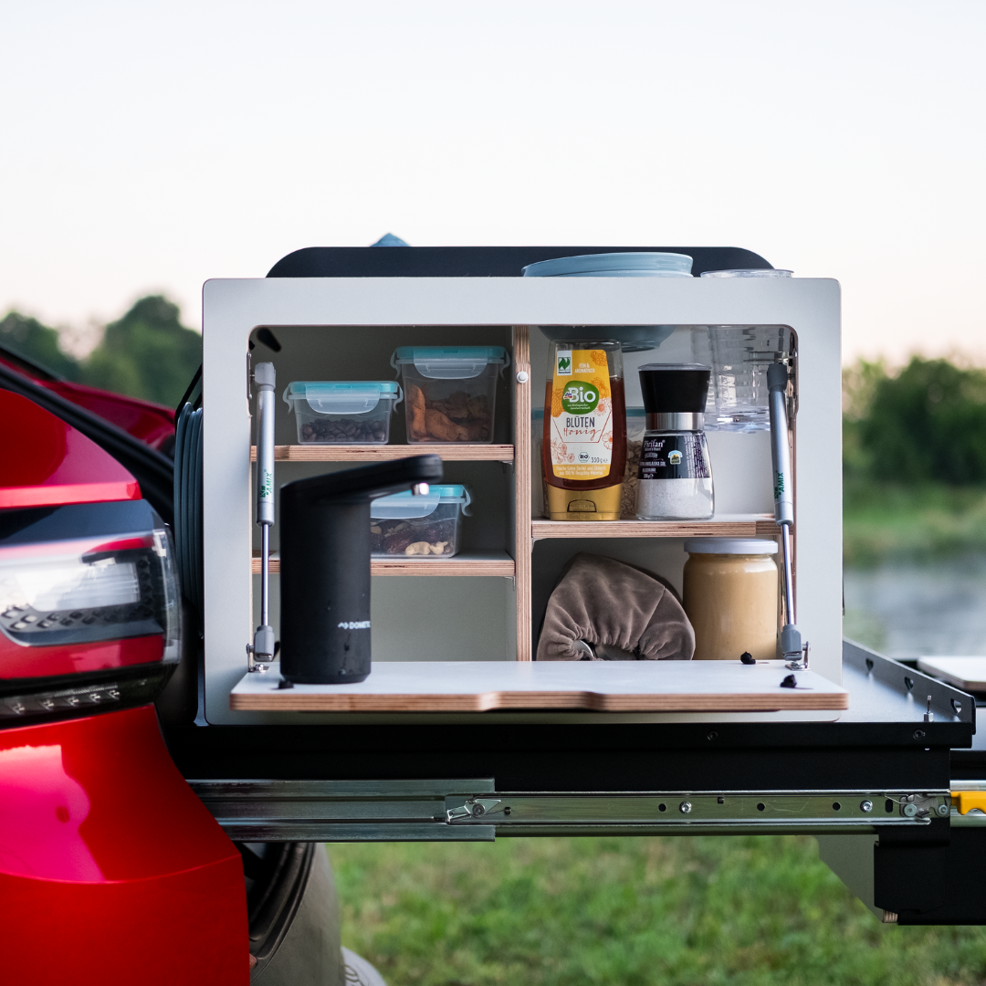 Campingbox in de kofferbak met Tupperbakjes en kruiden tijdens het camperen met de auto