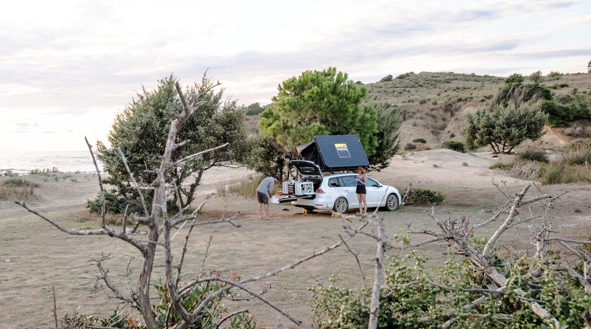 Sistema estraibile squiq con campingbox in spiaggia, in uso da parte di due persone con una station wagon