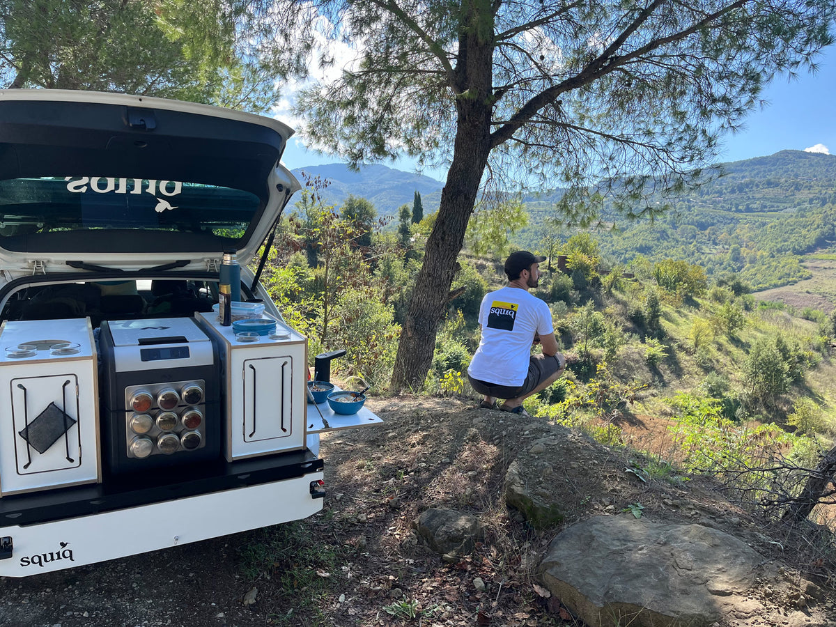 Campeggio con il sistema estraibile posteriore squiq-Traveler con cucina posteriore e campingbox; persona in maglietta squiq guarda in lontananza