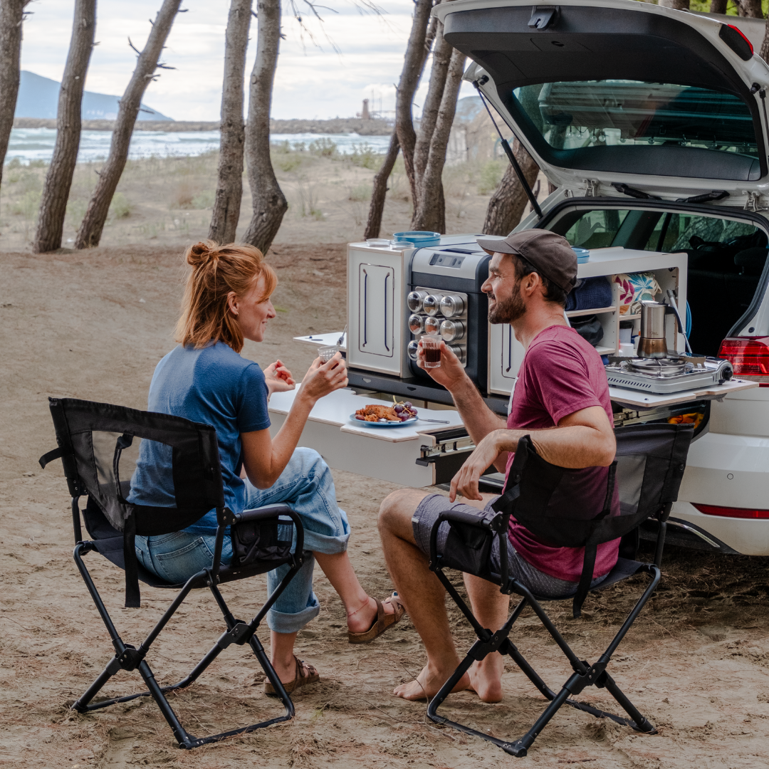 Zwei Personen trinken Kaffee vor einer Campingbox im Kofferraum ihres Autos mit Dachzelt und Mini Camper Ausbau