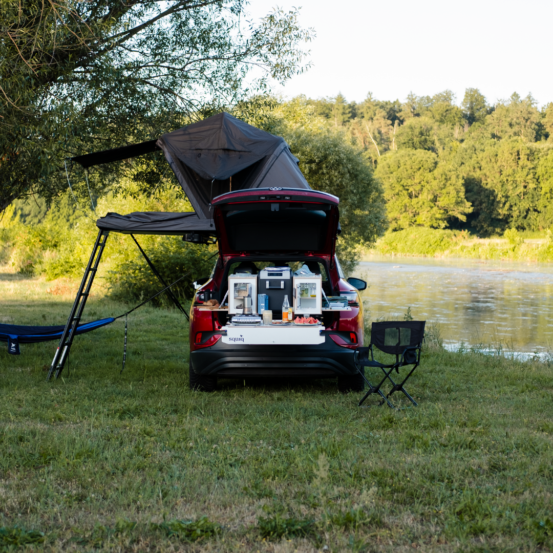 Campingbox in de kofferbak van de SUV met SQUIQ uitschuifsysteem, daktent en hangmat aan de rivier